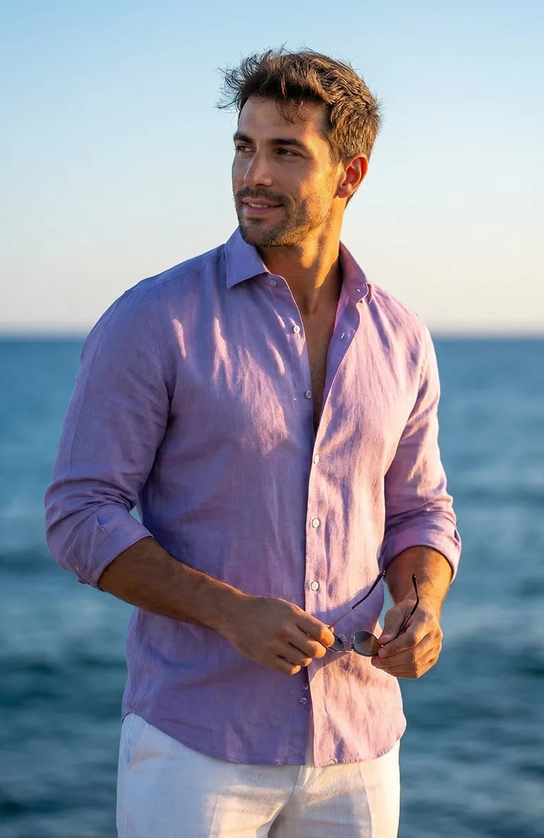 Man wearing a Purple Bradford shirt and white pants standing by the ocean.
